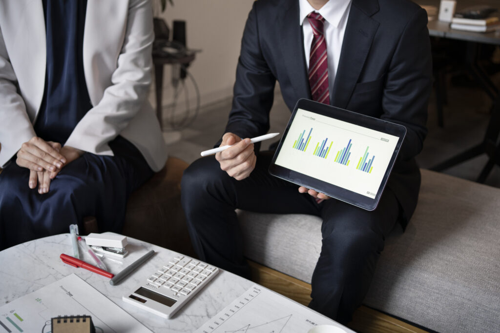 Businessman in a suit holding a digital tablet displaying bar graphs, explaining financial data analysis during a meeting.
