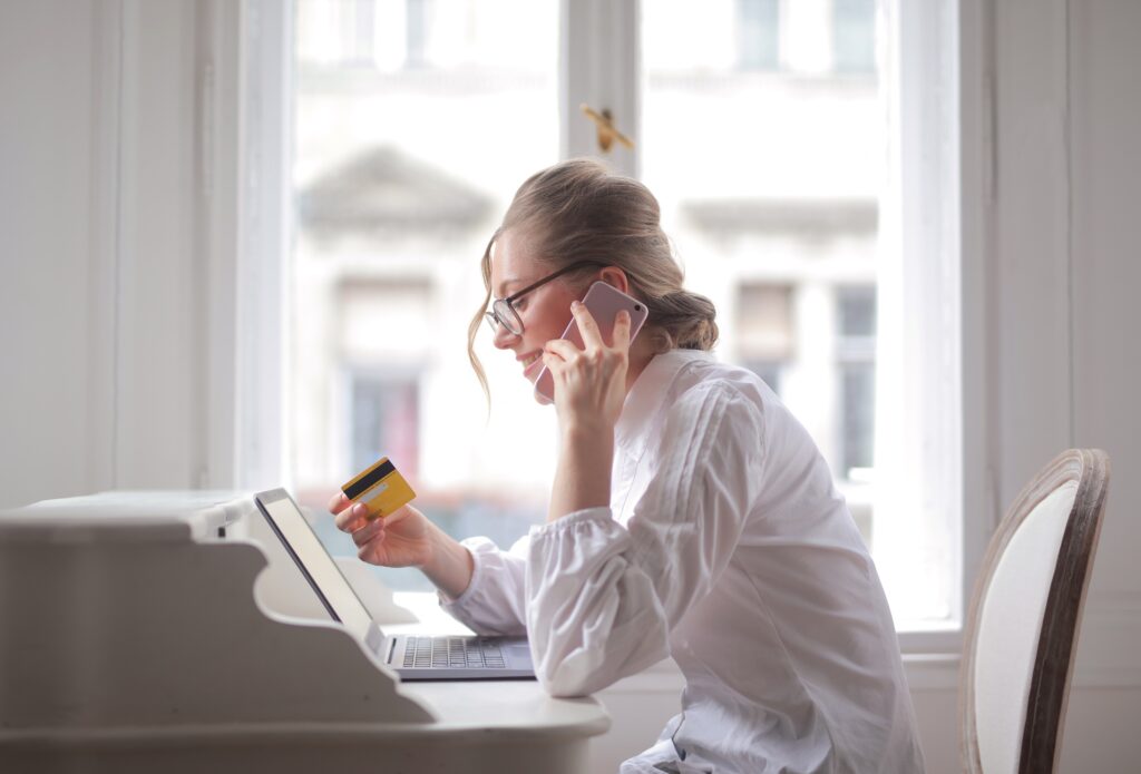 Woman using a laptop and holding a credit card while talking on the phone at home.