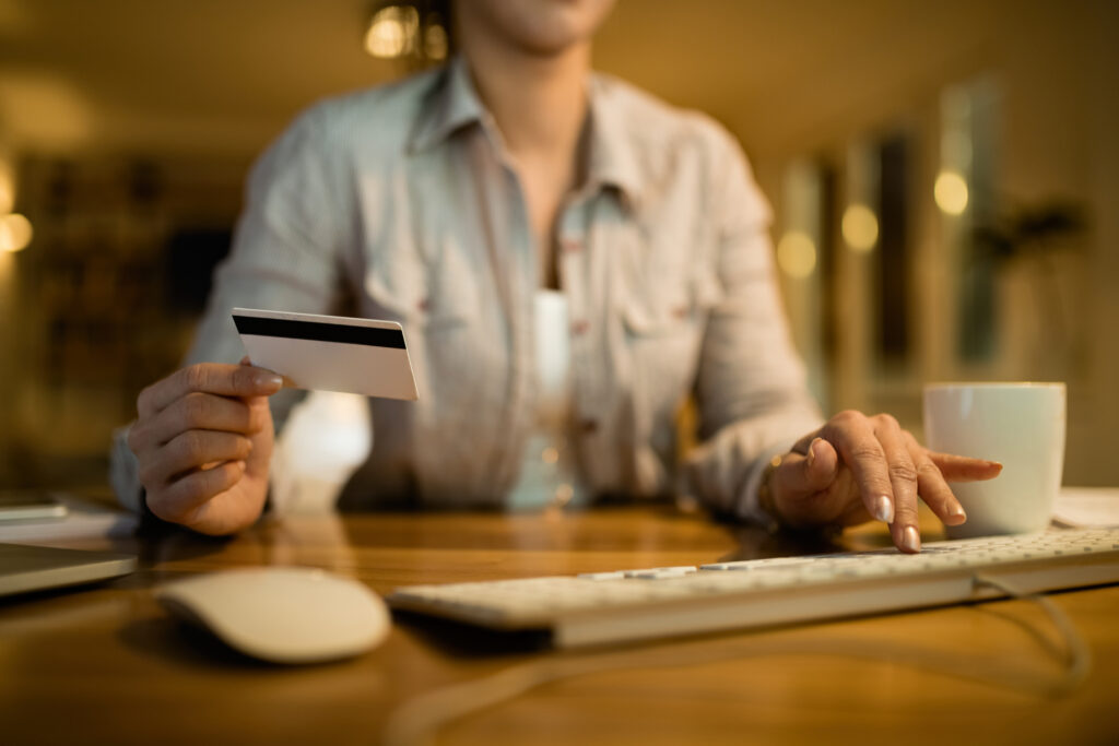 Woman holding a credit card while using a computer to make an online payment at night.
