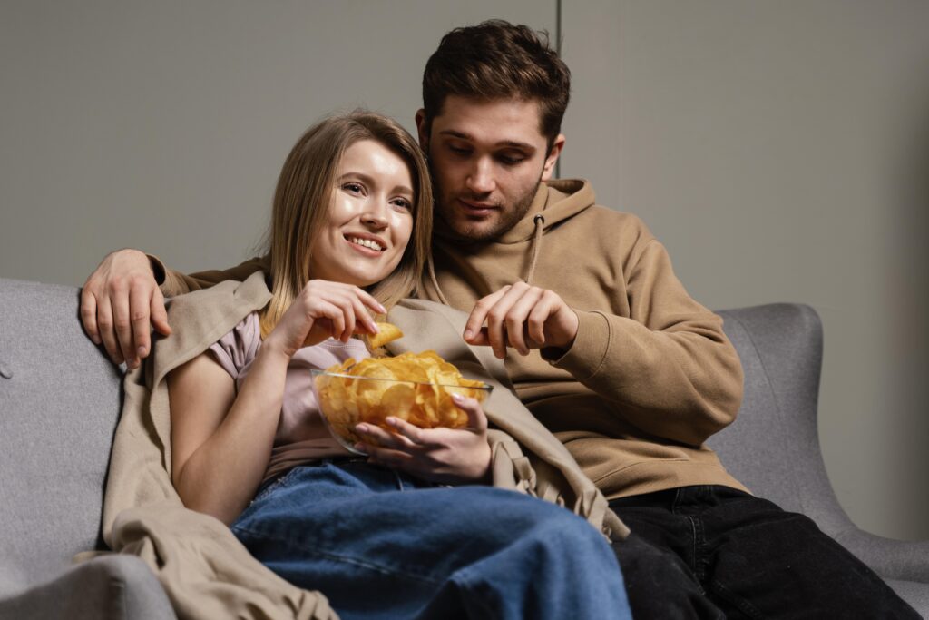 Couple on couch watching tv and eating chips