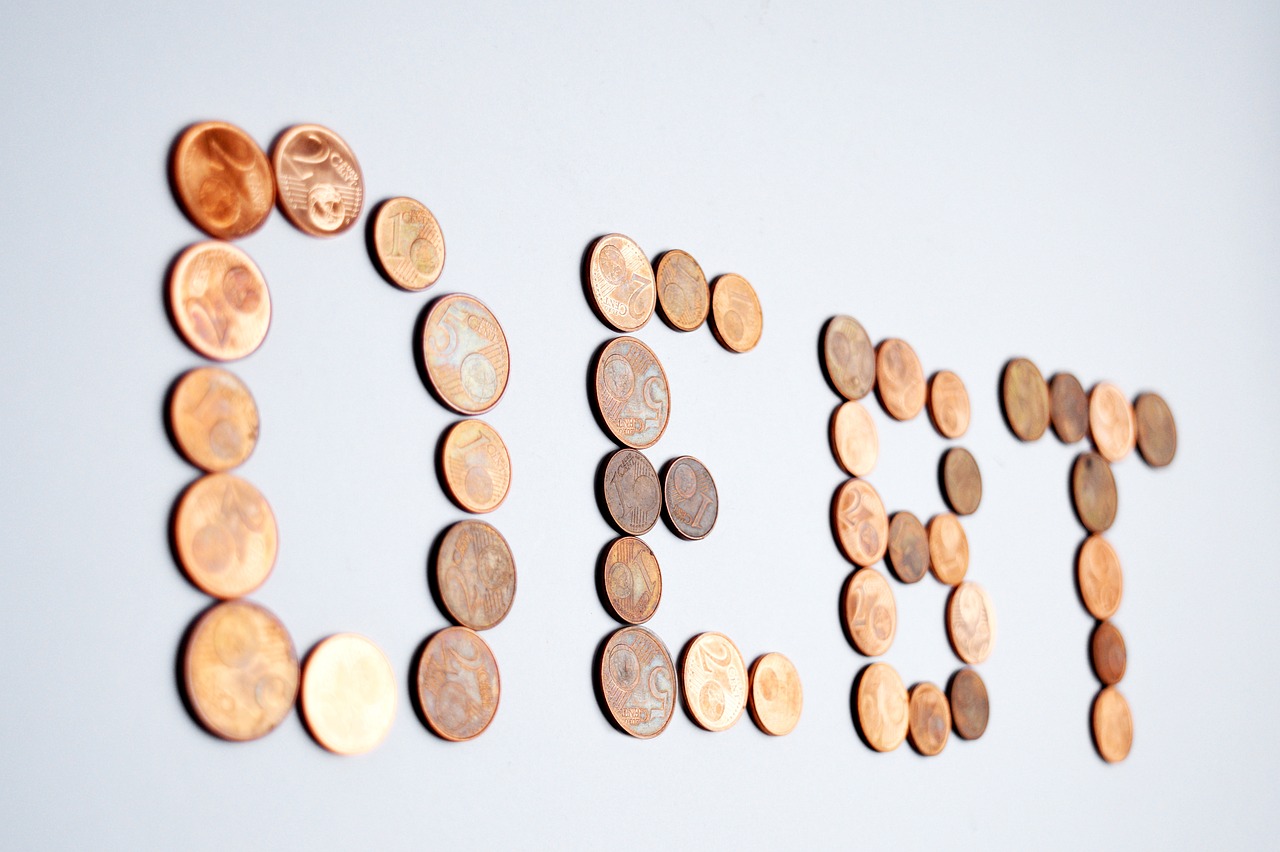 The word “DEBT” spelled out using copper coins on a white background.