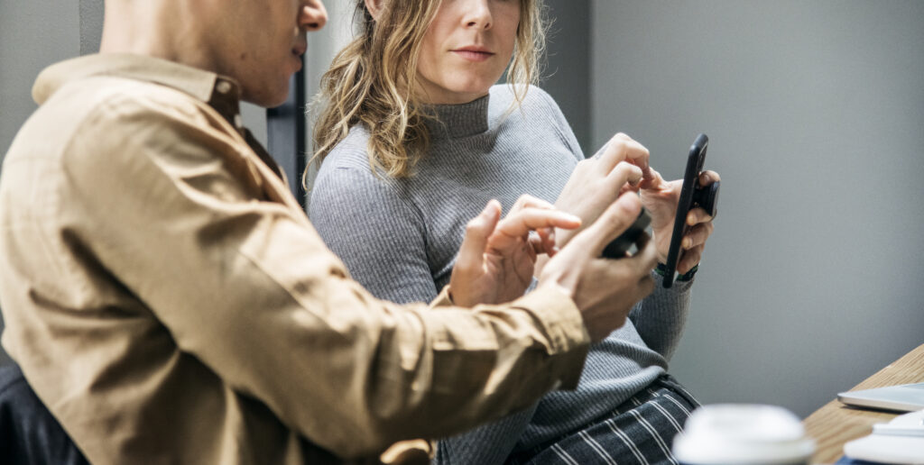 Two people sitting together and discussing something on their smartphones, suggesting financial planning or account decisions.
