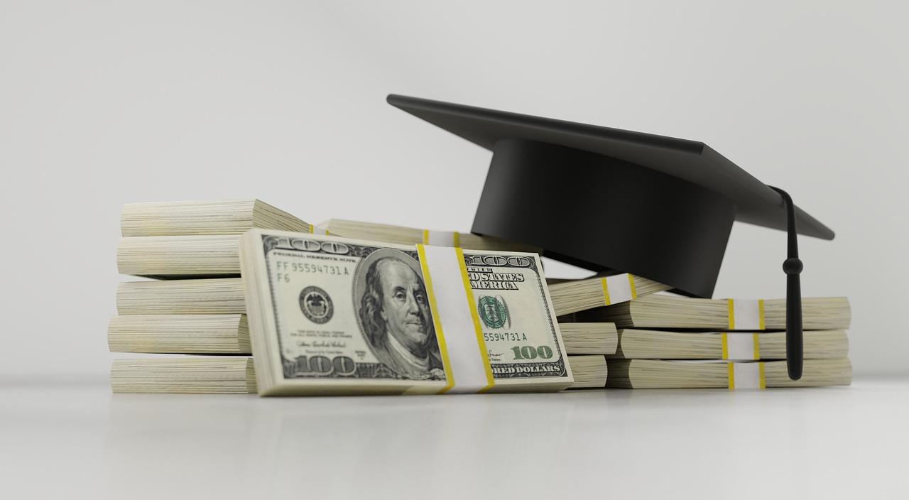 A graduation cap placed on stacks of hundred-dollar bills, symbolizing student loan debt and the cost of higher education.