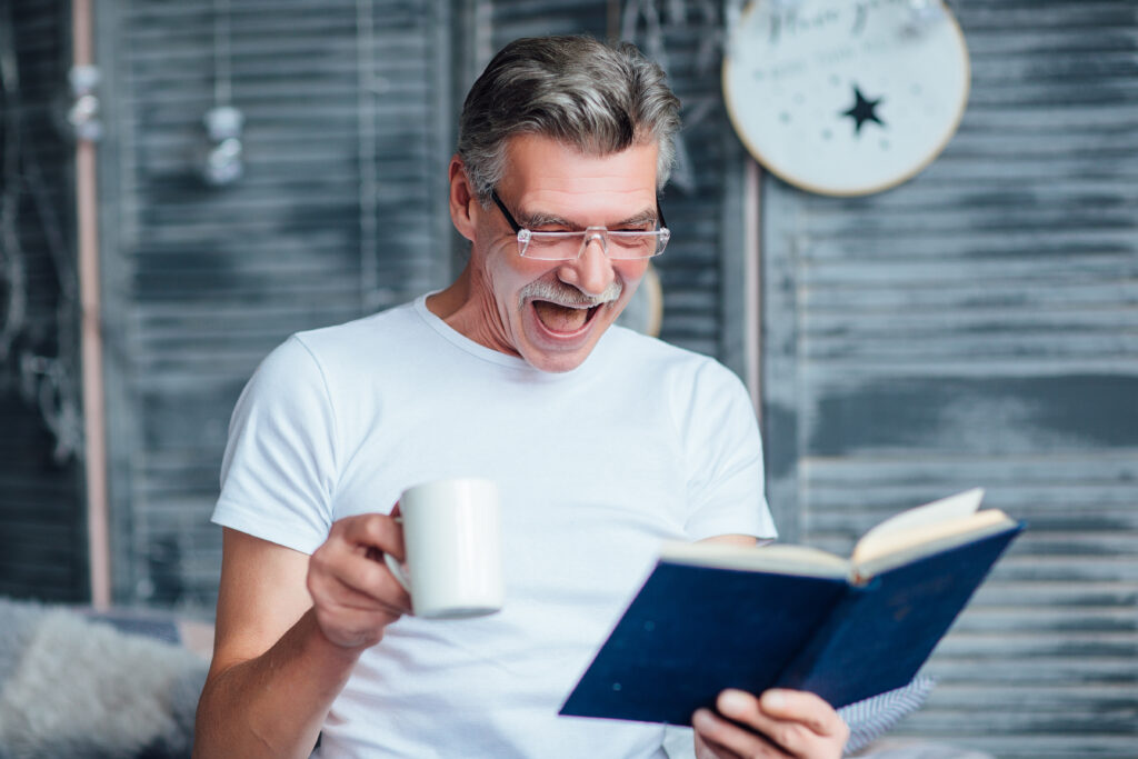 Portrait of eldery man sitting on bed , holding book, smiling happily !