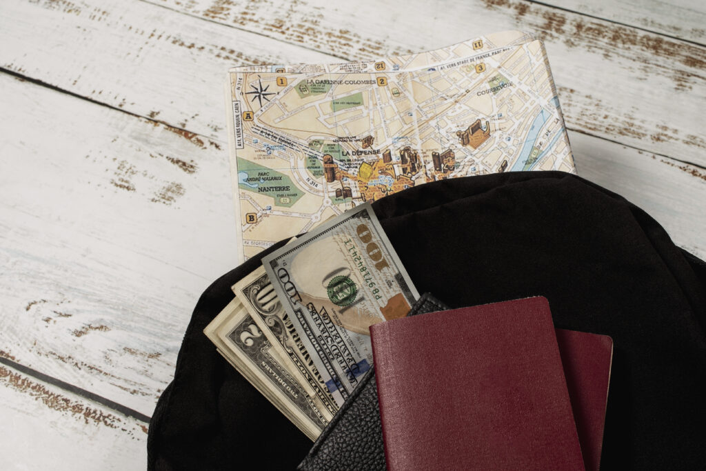 Open travel bag with US dollar bills, passports, and a city map on a wooden surface.