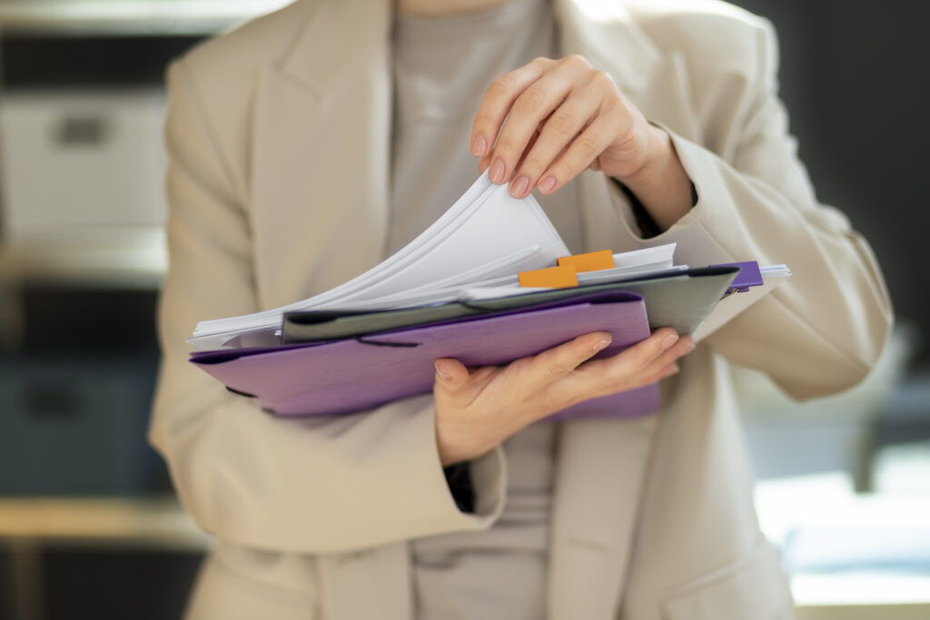 A businesswoman holding a stack of organized documents in folders, preparing paperwork for a loan application.