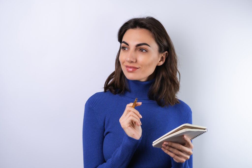Young woman in a blue golf turtleneck on a white background pensive with a notebook in her hand thinks about ideas, goals for the year